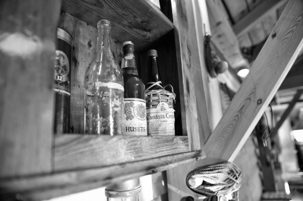 Old bottles and a woven flask on a wooden shelf inside the museum boathouse
