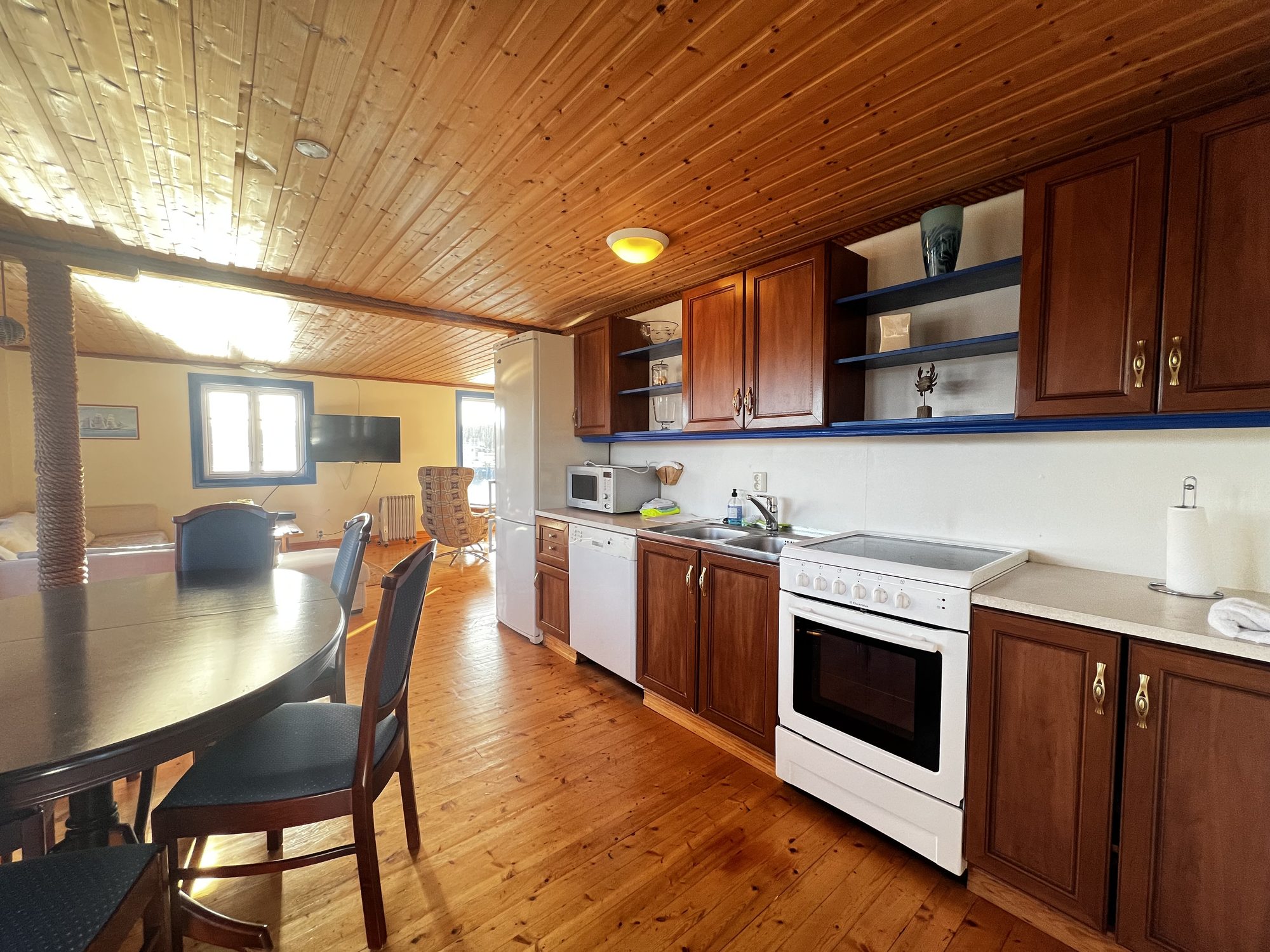 The Heritage — kitchen and dining area seen from the round table, with TV and sea-view windows beyond