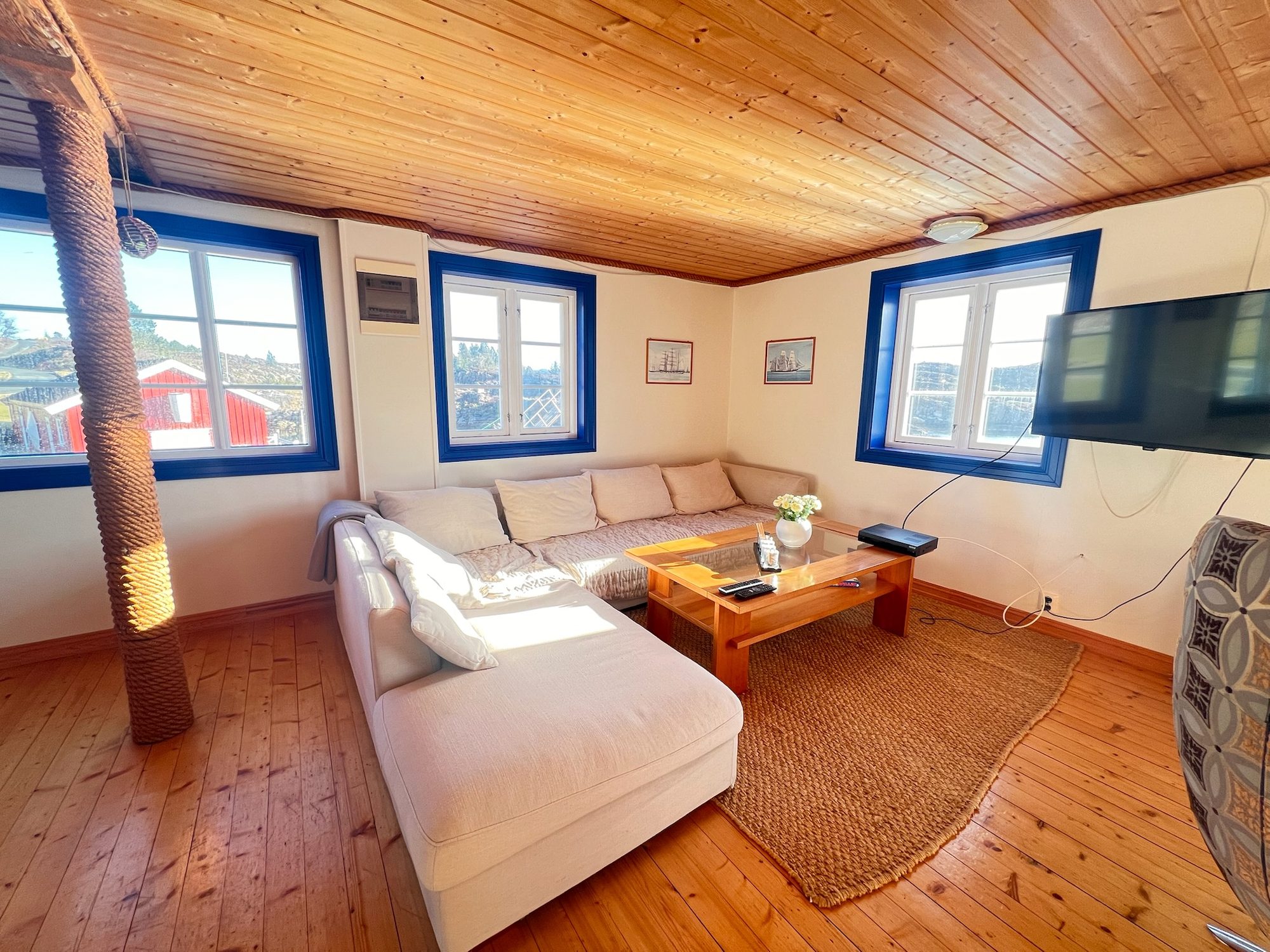 The Heritage — open-plan living room with corner sofa, rope-wrapped pillar and blue-framed windows