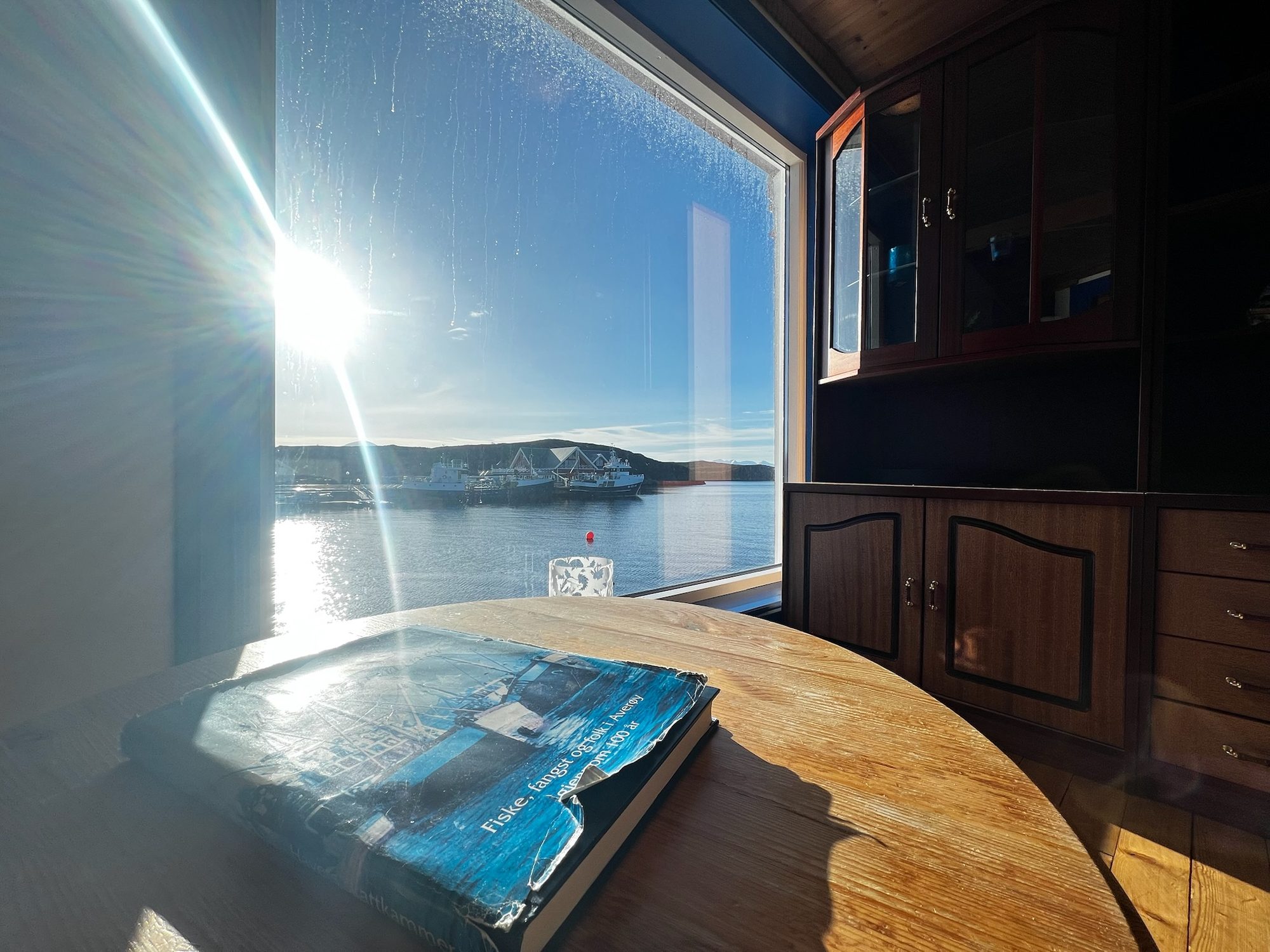 The Heritage — round table by the window with a book, harbour and fishing boats beyond